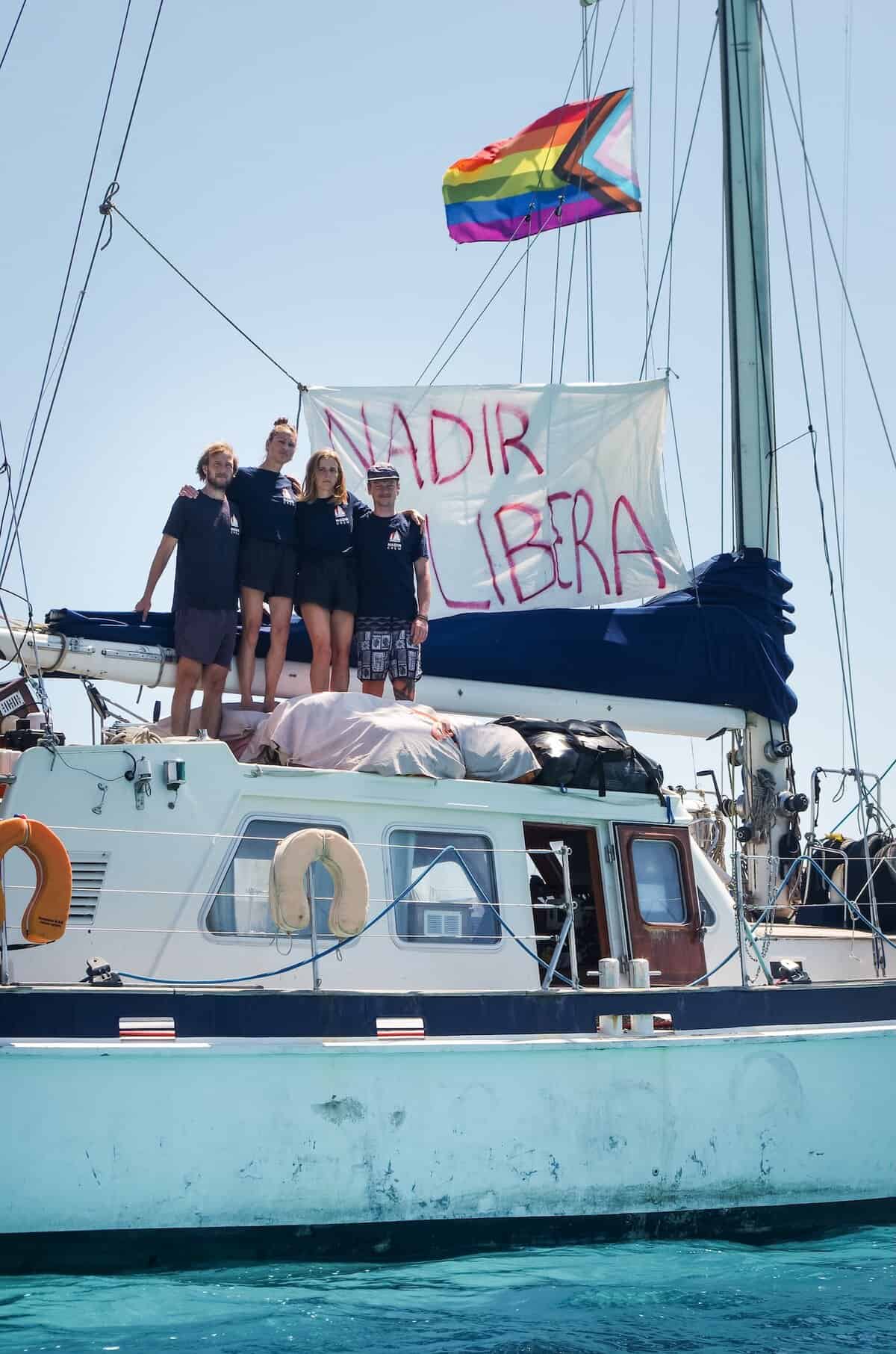 Die Crew der NADIR vor einem gehissten Banner mit der Aufschrift NADIR LIBERA
