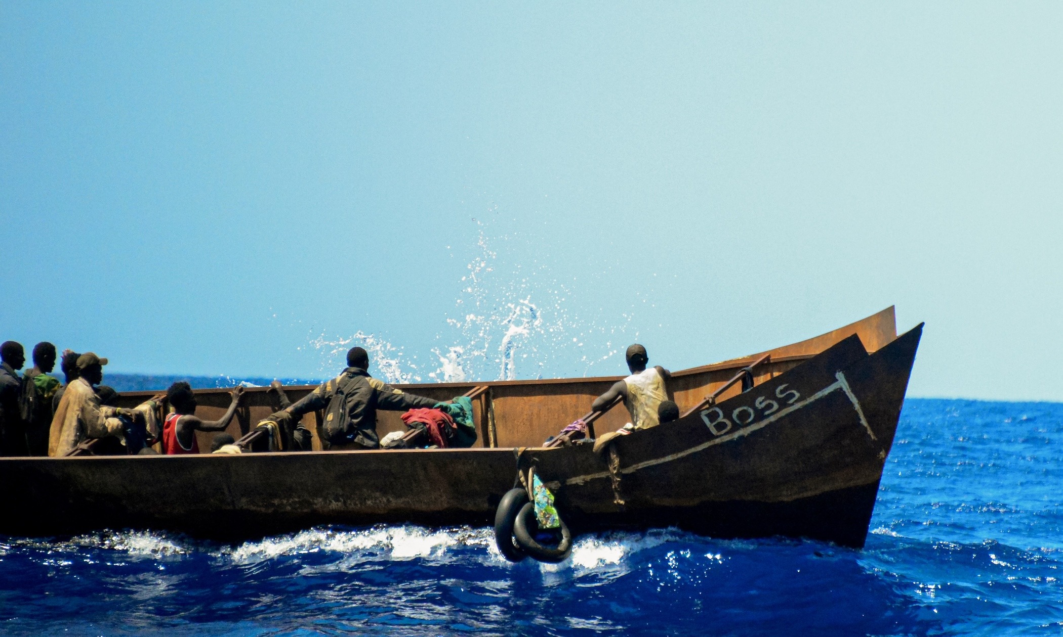 Auf einem sich stark auf den hohen Wellen  neigenden Eisenboot halten sich Geflüchtete fest, u, nicht ins Meer zufallen. Die Personen auf dem Eisenboot waren seit 6 Tagen unterwegs gewesenl, als die Crew der NADIR auf sie stieß.