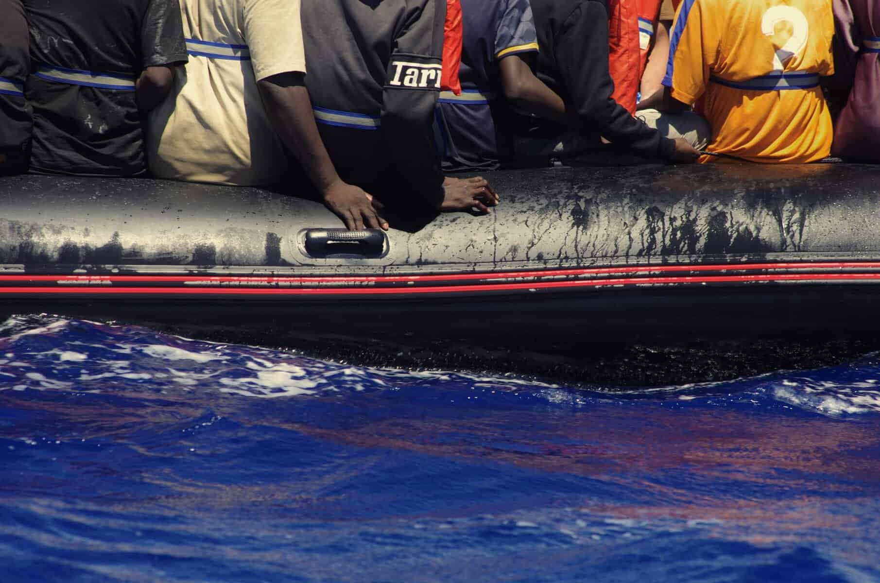 Menschen auf der Flucht sitzen dicht gedrängt auf einem Schlauchboot im offenen Meer.