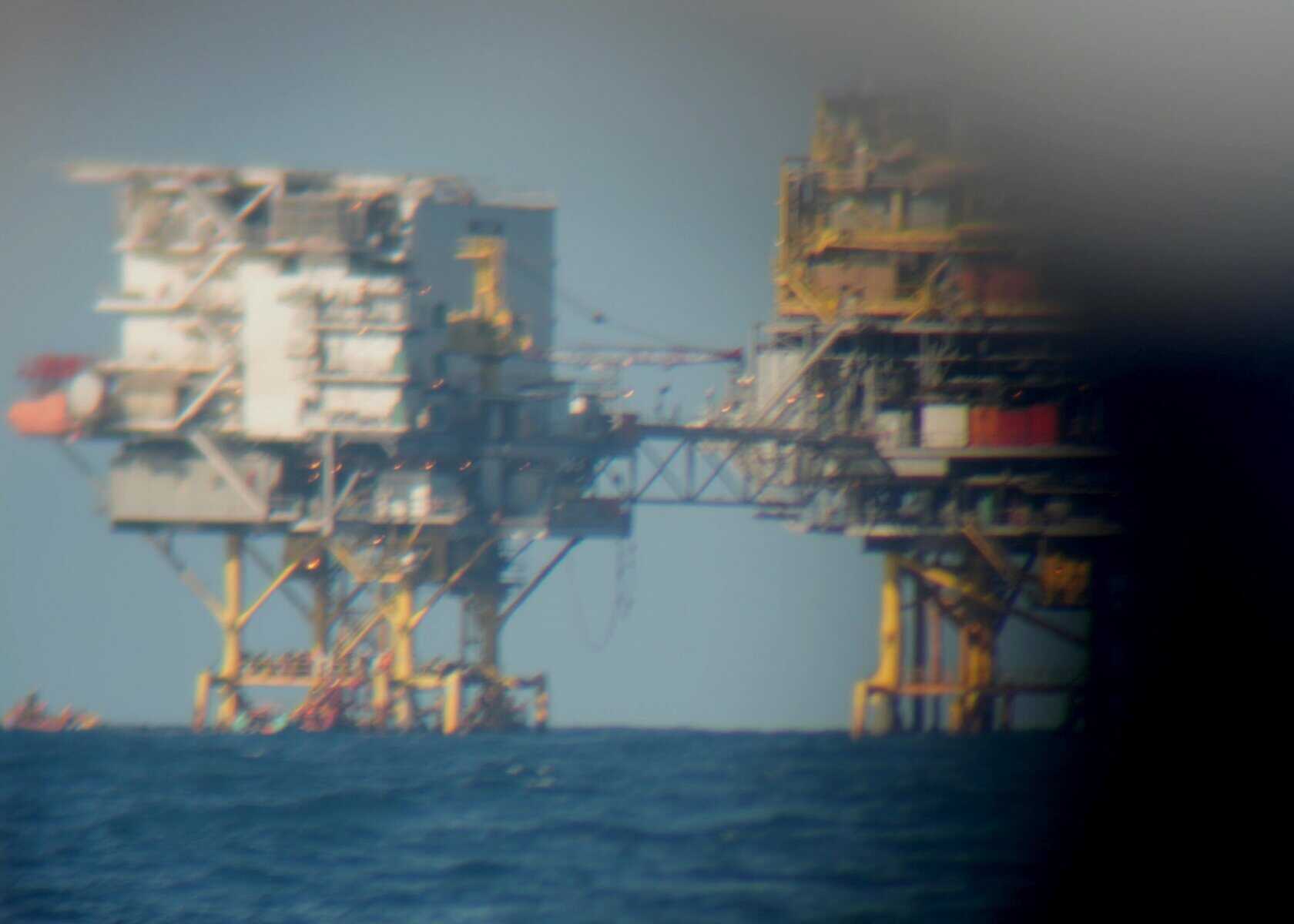 Blick durch ein Fernglas: Gasplattform Miskar im Meer, bestehend aus zwei verbundenen Anlagen auf Stelzen über dem Wasser.