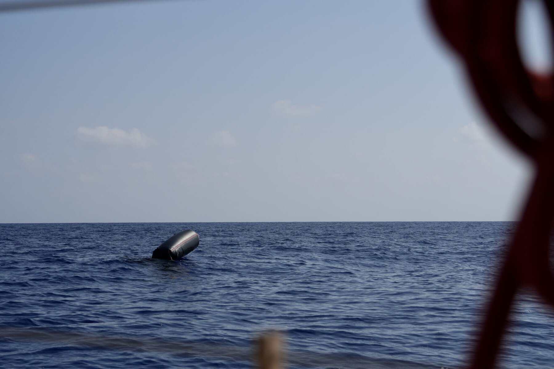 Gekentertes Schlauchboot treibt im offenen Meer unter klarem Himmel.