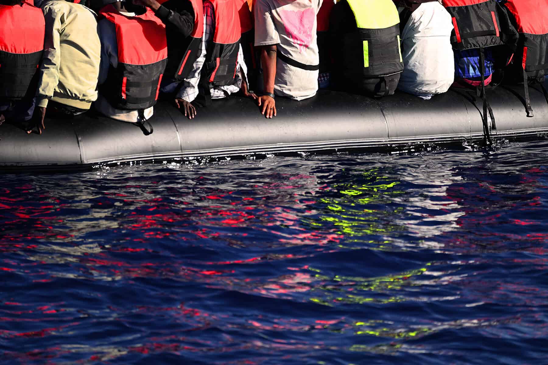 Menschen mit Schwimmwesten sitzen auf einem Schlauchboot im Meer