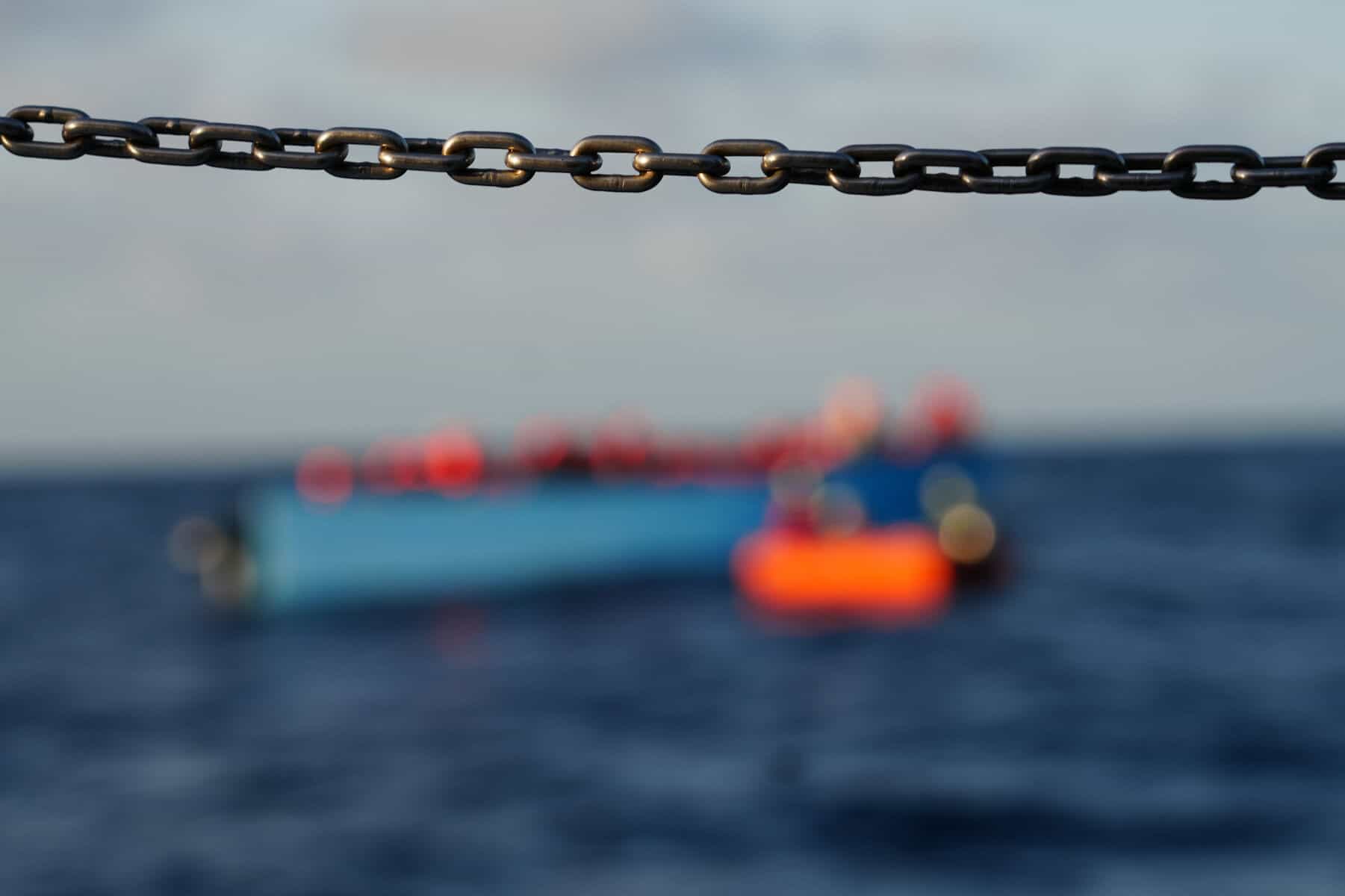 Boot mit Geflüchteten am Meer hinter einer Kette scharf abgeblendet.