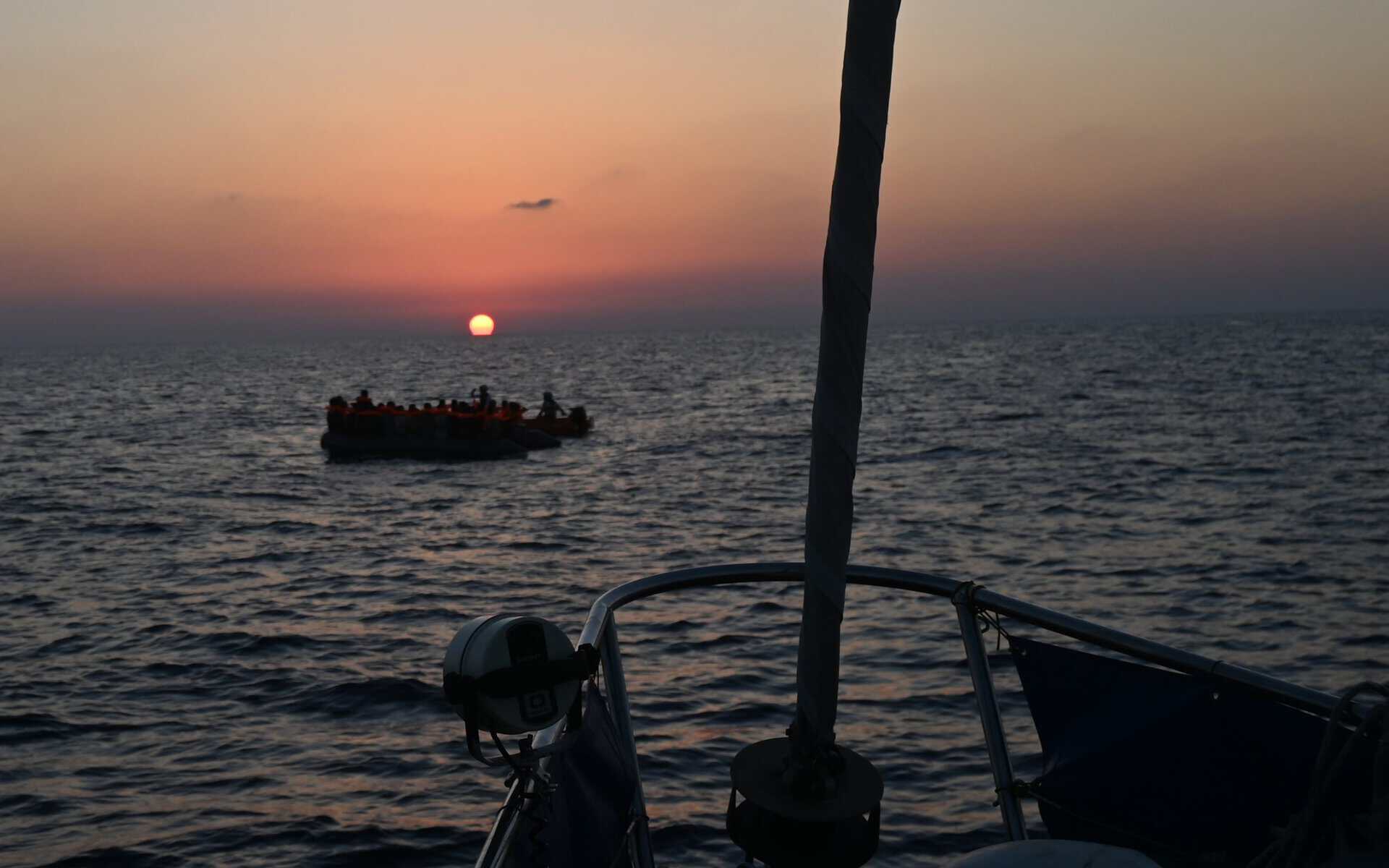 Boot mit mehreren Personen auf der Flucht auf dem Meer bei Sonnenuntergang, aufgenommen von NADIR aus.