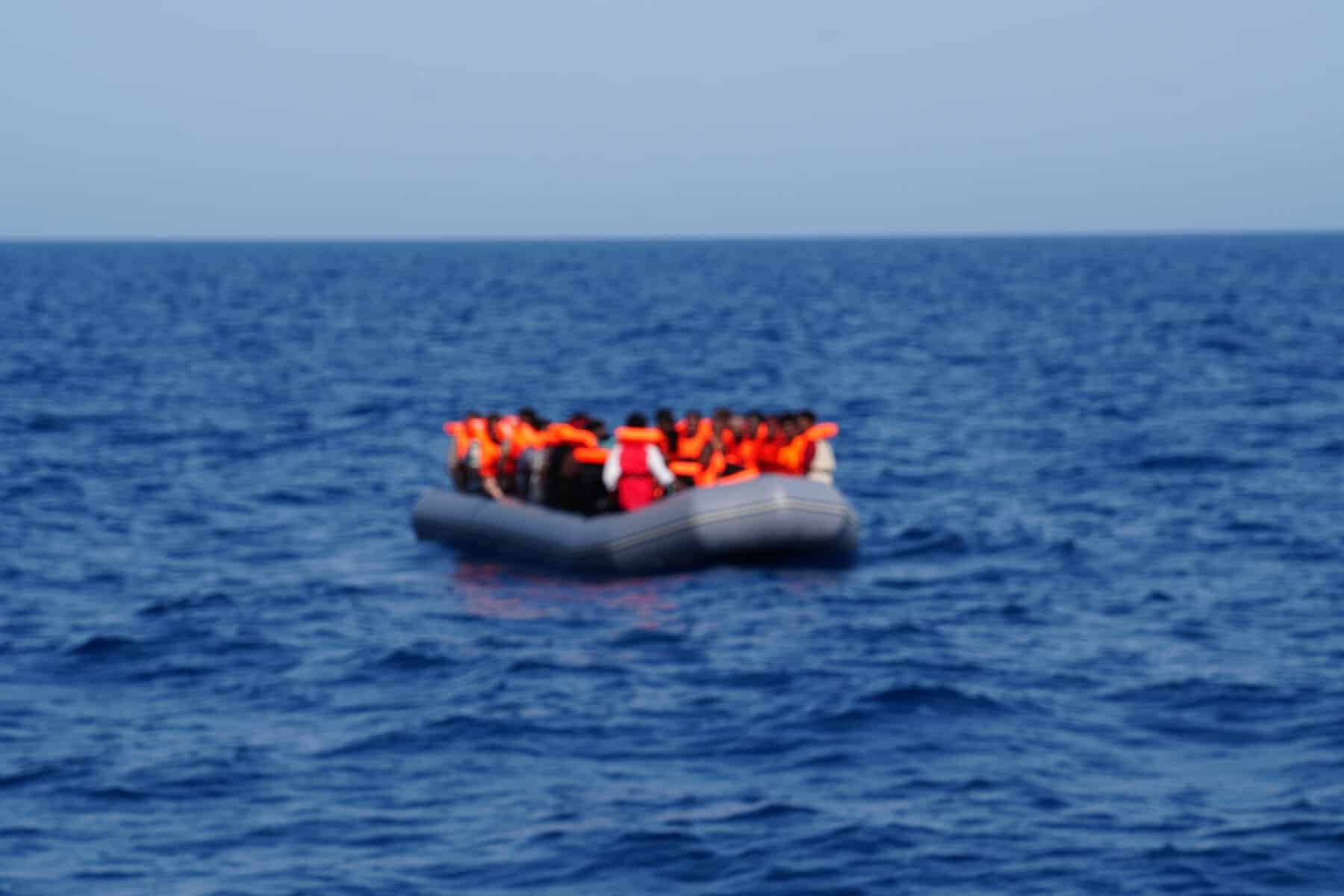 Schlauchboot mit mehreren Menschen auf der Flucht in orangefarbenen Rettungswesten auf dem Meer.