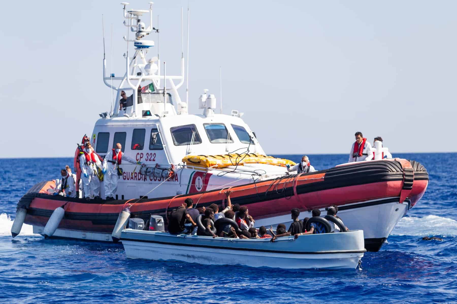 Schiff der Italienische Küstenwache davor ein Boot mit Menschen auf der Flucht
