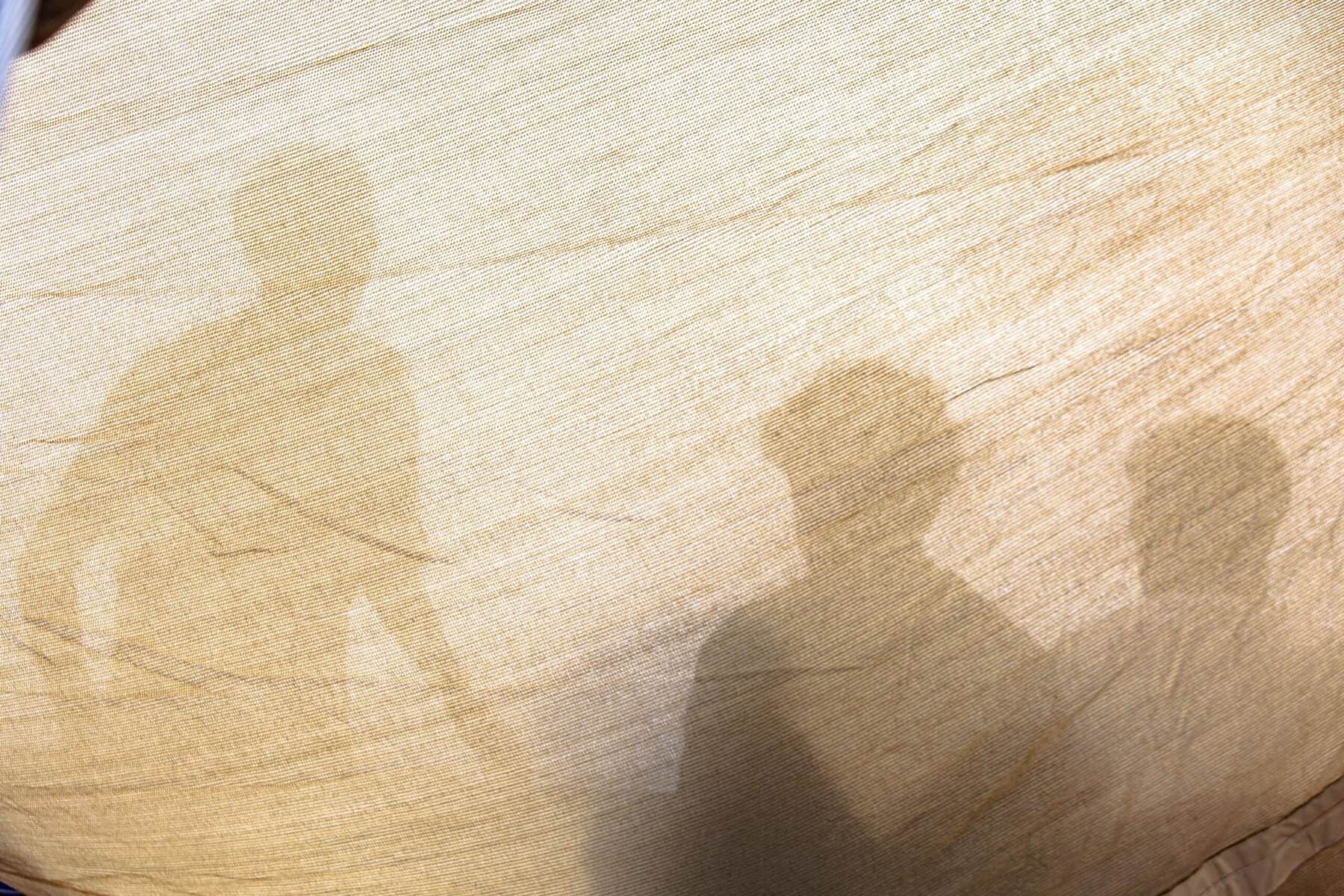 Beige Stofffläche mit mehreren schemenhaft durch den Stoff erkennbaren Personen.